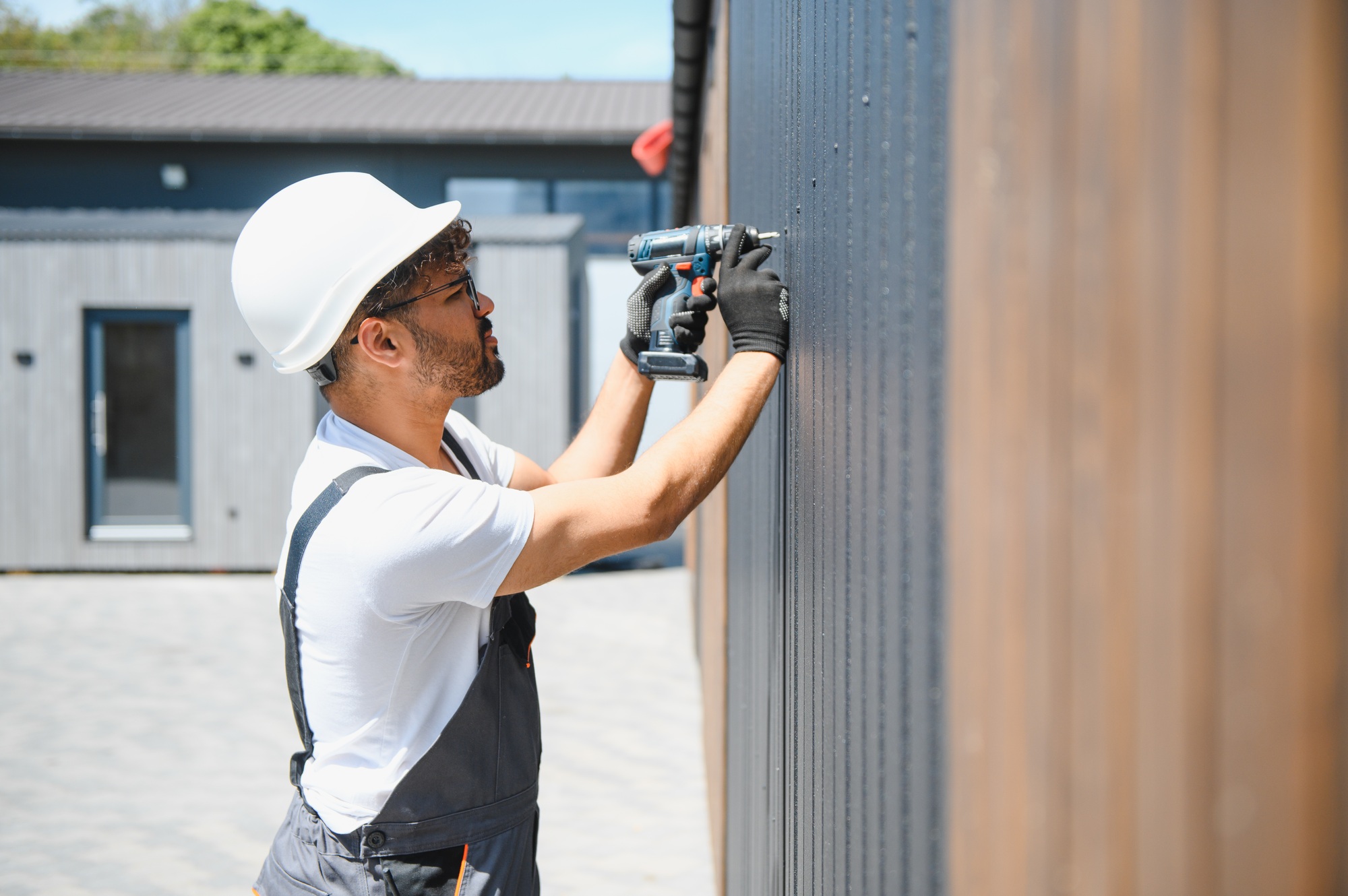 Construction worker using cordless drill installing siding on prefabricated building